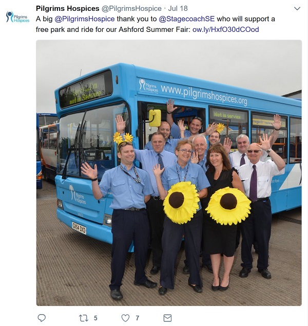 Smiling and waving staff in front of a bus with giant sunflowers