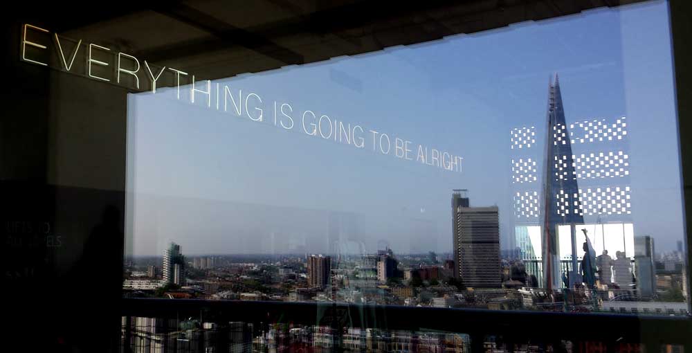 artwork in the Tate - Neon sign says 'Everything is going to be alright'. Reflections of the London skyline on a window. 