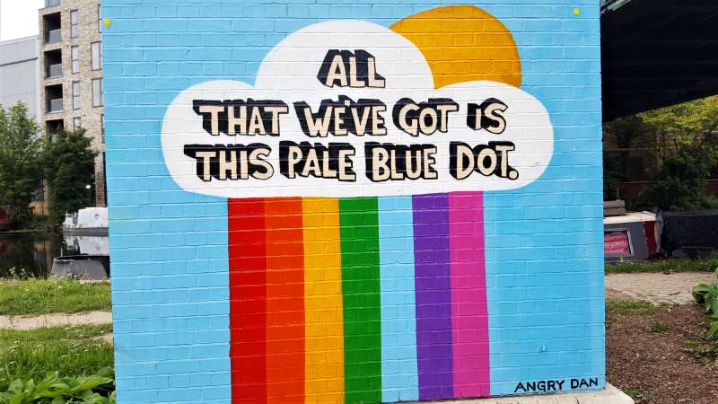 street art. a rainbow with the text which says - all that we've got is this pale blue dot. By Angry Dan